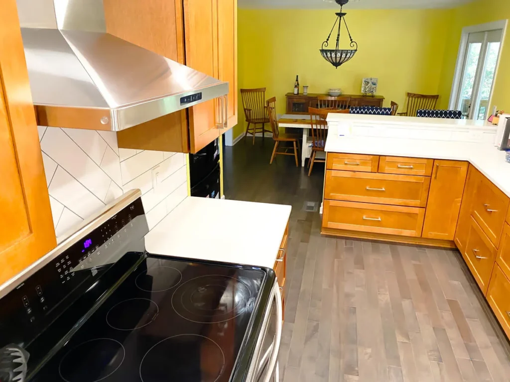 Kitchen cooking area with electric stove, range hood, wooden cabinets, and open layout to dining area
