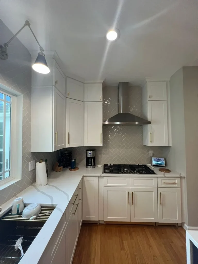 Kitchen cooktop with stainless steel range hood and herringbone tile backsplash in white kitchen