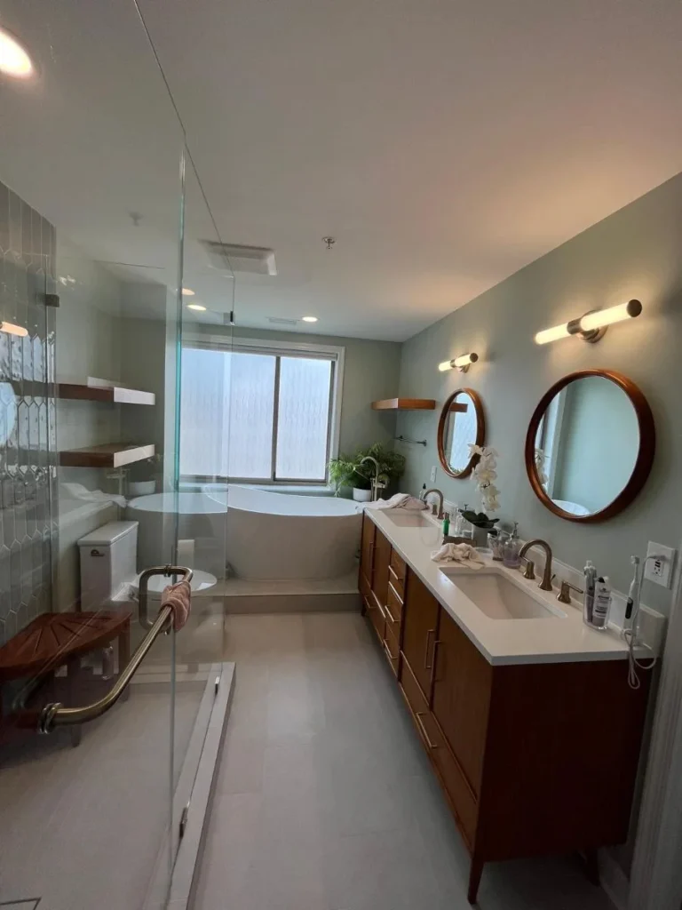 Modern bathroom with double vanity, round mirrors, walk-in shower, and bathtub by window