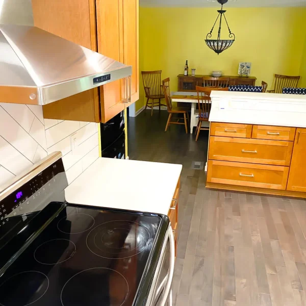 Kitchen cooking area with electric stove, range hood, wooden cabinets, and open layout to dining area