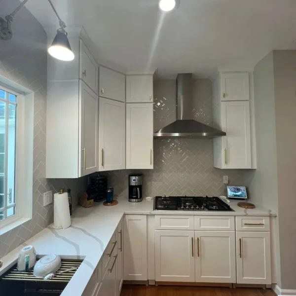 Kitchen cooktop with stainless steel range hood and herringbone tile backsplash in white kitchen