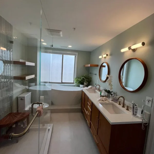 Modern bathroom with double vanity, round mirrors, walk-in shower, and bathtub by window