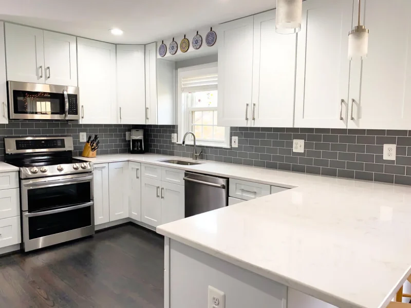 Modern U-shaped kitchen with white cabinets, gray subway tile backsplash, quartz countertops and stainless steel appliances